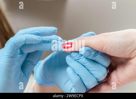 Il manicurista in guanti blu strofina l'olio cuticolo in un dito dopo la manicure nel salone di bellezza. Foto Stock