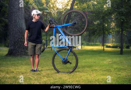 Giovane uomo sportivo con casco da bicicletta e occhiali che tiene la sua bici nel parco. Sport e tempo libero. Foto Stock