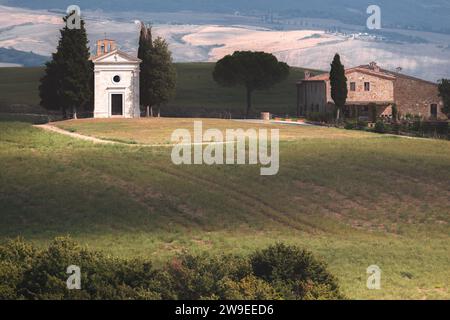 La piccola e affascinante Cappella bianca Vitaleta nel paesaggio paesaggistico di campagna delle dolci colline della Val d'Orcia nella campagna toscana, Italia. Foto Stock