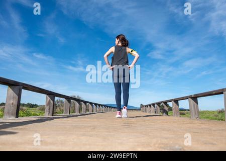 Donna sportiva su una passerella di legno che si prepara a correre, vista posteriore Foto Stock