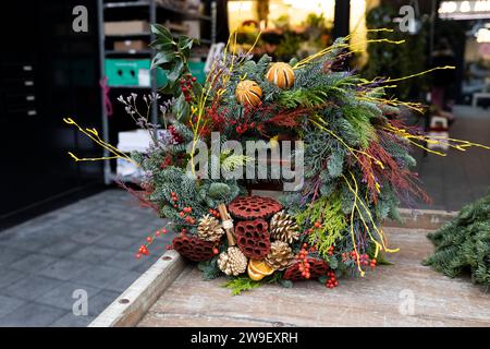 Corona di Natale in abete, decorata con mandarini secchi, loto, erbe, frutti di bosco nei toni verde e arancione in vendita al mercato. Foto Stock