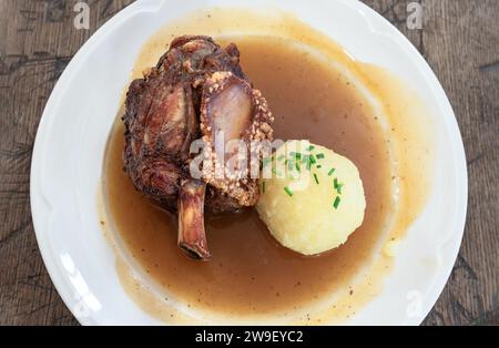 Un'intera noce di maiale arrosto servita con sugo di birra scura fatto in casa e gnocchi di patate su piatto di ceramica. Vista dall'alto, spazio per testo, messa a fuoco selettiva Foto Stock