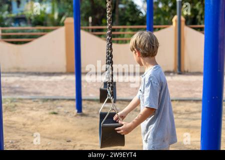 Un bambino in età prescolare premuroso, si trova vicino all'altalena, come se decidesse se provare a dondolare su di loro. Foto Stock