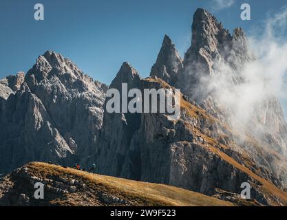 Un gruppo eterogeneo di persone che camminano su un unico file lungo un tortuoso sentiero di montagna, con una maestosa e aspra catena montuosa sullo sfondo Foto Stock