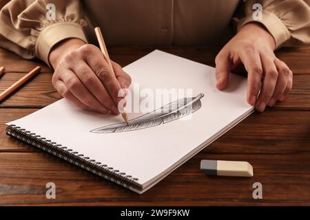 Donna che disegna piume con matita di grafite in un quaderno di bozzetti al tavolo di legno, primo piano Foto Stock