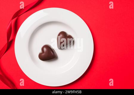 Due dolci al cioccolato a forma di cuore sul piatto su sfondo rosso, dolcetti di San Valentino Foto Stock