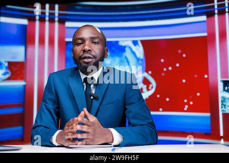 Anchorman che presenta gli ultimi eventi sul canale televisivo globale, che tratta argomenti quotidiani riguardanti la popolazione e il dramma delle celebrità. Giornalista afroamericano che trasmette informazioni, contenuti tv. Foto Stock