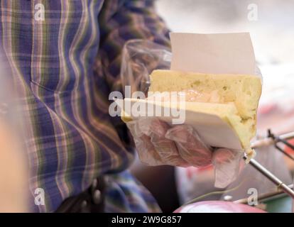 Le mani di un commerciante maschile che raccoglie il gelato con gocce di cioccolato alla vaniglia nel pane per un cliente. Foto Stock