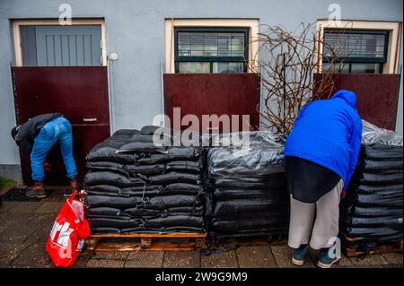 Deventer, Paesi Bassi. 27 dicembre 2023. Si vedono due persone che mettono sacchi di sabbia davanti a una casa per proteggerla dall'acqua alta. A causa dell'innalzamento dell'acqua nel fiume IJssel, il comune del Deventer sta posizionando sacchi di sabbia sulla banchina per proteggere il centro storico della città. Le forti piogge che sono cadute in questi ultimi mesi, unite al fatto che le Alpi sono insolitamente calde per questo periodo dell'anno, hanno creato il fiume IJssel che inonda a Overijssel, Gelderland, Drenthe, Brabante e Limburgo. (Foto di Ana Fernandez/SOPA Images/Sipa USA) credito: SIPA USA/Alamy Live News Foto Stock