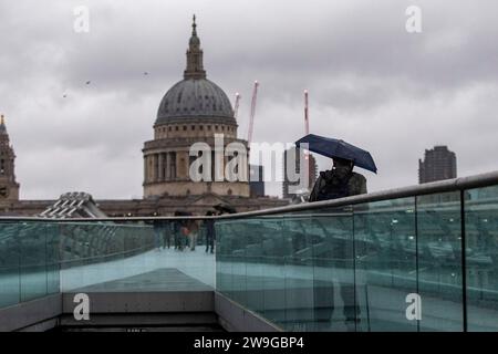 La gente affronta il tempo attraversando il Millennium Bridge a Londra. La tempesta Gerrit porterà venti forti e piogge pesanti in molte parti del Regno Unito mercoledì, con probabili rischi di vento, avvertiti i previsione. Data foto: Mercoledì 27 dicembre 2023. Foto Stock