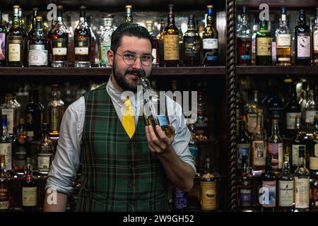 Bar man che nozza una bottiglia di whisky al Bertie's Whisky Bar, Fife Arms, Braemar, Scozia. Foto Stock