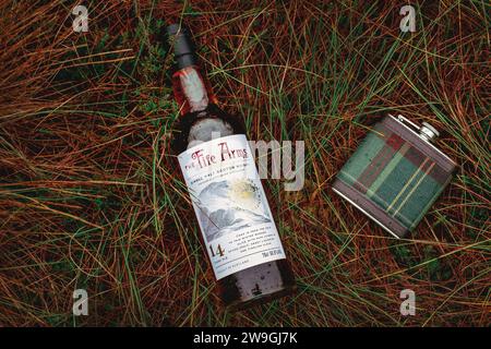 Fiasca per anca tartan con bottiglia Single Malt Scotch Whisky appoggiata sull'erba. Foto Stock