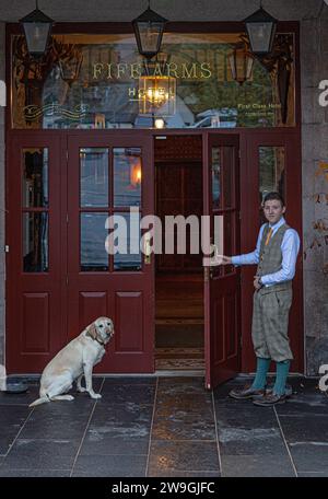 Giovane portiere dell'hotel apre la porta al Fife Arms Hotel a Breamer, Aberdeenshire, Scozia. Foto Stock