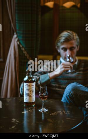 Un giovane maschio seduto in poltrona che noce whisky single malt nel bicchiere. Foto Stock