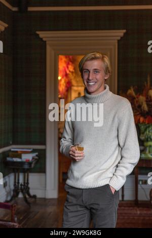 Elegante e affascinante giovane uomo caucasico che si gode il whisky in una camera elegante. Foto Stock