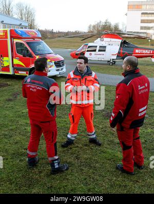 Rostock, Germania. 28 dicembre 2023. Marc Marrone (l-r), pilota, Christian Manshen, paramedico di emergenza a Johanniter-Unfall-Hilfe e.V., e Dion Gabteni, paramedico di emergenza, parlano davanti a un'ambulanza e l'elicottero di salvataggio Johanniter a Klinikum Südstadt. Crediti: Bernd Wüstneck/dpa/Alamy Live News Foto Stock