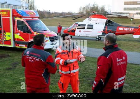 Rostock, Germania. 28 dicembre 2023. Marc Marrone (l-r), pilota, Christian Manshen, paramedico di emergenza a Johanniter-Unfall-Hilfe e.V., e Dion Gabteni, paramedico di emergenza, parlano davanti a un'ambulanza e l'elicottero di salvataggio Johanniter a Klinikum Südstadt. Crediti: Bernd Wüstneck/dpa/Alamy Live News Foto Stock