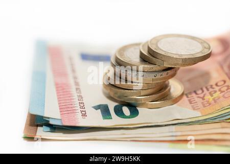 Primo piano di diverse banconote in euro impilate l'una sopra l'altra. Le monete in euro sono in cima. Lo sfondo è di colore chiaro. Foto Stock
