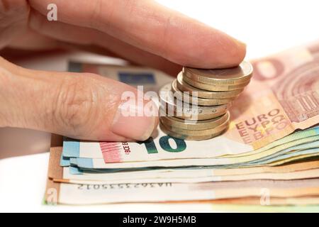 Primo piano di diverse banconote in euro impilate l'una sopra l'altra. Una mano cerca qualche moneta che giace sopra il denaro. Foto Stock