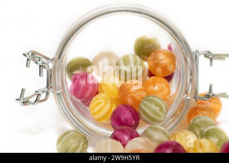 Vista ravvicinata di un barattolo da portata con palline di zucchero colorate. Le palline di zucchero si estraggono da un recipiente con coperchio. Lo sfondo è di colore chiaro. Foto Stock