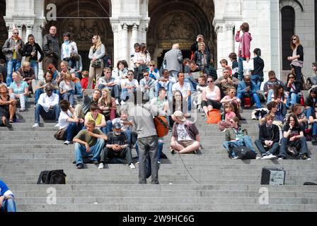 Busker si esibisce con una folla di giovani seduti sui gradini della Basilica del Sacro cuore, Parigi, Francia Foto Stock