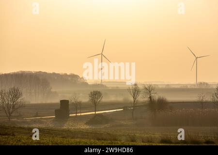 Due turbine eoliche si stagliano contro un cielo arancione all'alba. Foto Stock