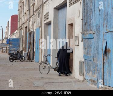 L'uomo esce da un albergo fatiscente con porte in legno blu e biciclette a Essaouira, Marocco. 28 dicembre 2023 Foto Stock