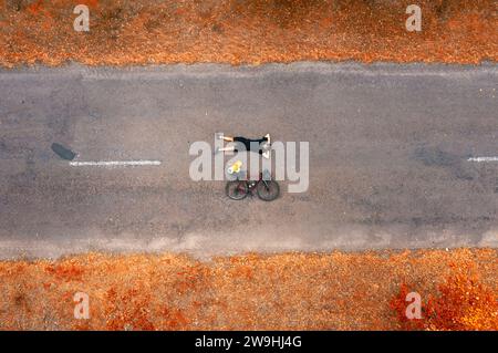 Vista dall'alto di un ciclista con una bici da strada sdraiata sull'asfalto. Libertà e viaggi. Foto Stock