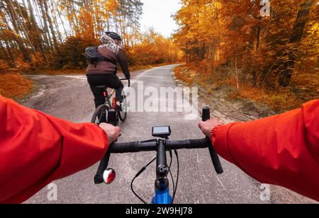 I ciclisti in bicicletta viaggiano lungo la strada nella foresta autunnale. POV. Autunno in bicicletta nella foresta. Foto Stock