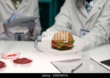 Un lavoratore di laboratorio non riconoscibile che tiene il piatto con hamburger di carne artificiale Foto Stock