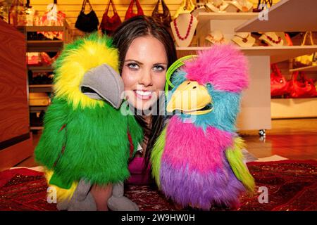 All'interno di un negozio boutique, una donna glamour si diverte a modellare giocando con i pupazzi di guanti a Dundee, in Scozia Foto Stock