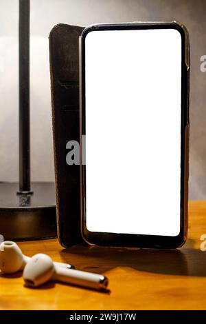 Smartphone con custodia ribaltabile e schermo bianco vuoto sul comodino, percorso di ritaglio Foto Stock