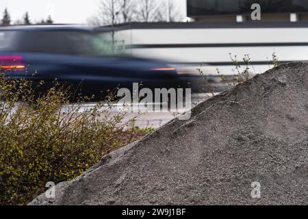 Cumulo di ghiaia vicino a una strada con un'auto sfocata sullo sfondo. Foto Stock