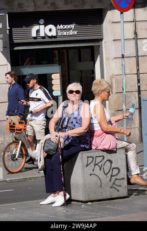 Barcellona, Spagna - 26 maggio 2022: Due donne anziane approfittano di una nappina sul viale per sedersi e idratarsi, mentre aspettano davanti a un Foto Stock