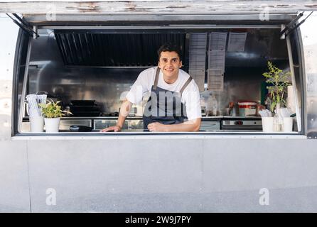 Ritratto di un giovane proprietario di un camion alimentare. Il proprietario di un food truck attende i clienti. Foto Stock