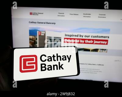 Persona che possiede uno smartphone con il logo dell'azienda statunitense Cathay General Bancorp (Cathay Bank) davanti al sito Web. Concentrarsi sul display del telefono. Foto Stock
