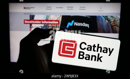Persona che possiede un telefono cellulare con il logo della società americana Cathay General Bancorp (Cathay Bank) davanti alla pagina Web. Concentrarsi sul display del telefono. Foto Stock