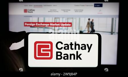 Persona in possesso di un cellulare con il logo della società statunitense Cathay General Bancorp (Cathay Bank) davanti alla pagina Web aziendale. Concentrarsi sul display del telefono. Foto Stock