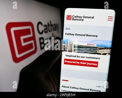 Persona che possiede uno smartphone con la pagina Web dell'azienda statunitense Cathay General Bancorp (Cathay Bank) davanti al logo. Concentrarsi sul centro del display del telefono. Foto Stock