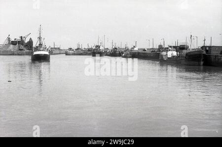 1972, storico, vista dei moli di Fleetwood, Lancs, Inghilterra, Regno Unito, che mostra un peschereccio che entra nel porto e alcuni altri ormeggiati. La città costiera di Fleetwood, nella contea di Wyre, era una volta uno dei più grandi porti di pesca del Regno Unito, con una grande flotta oceanica, ma il declino dell'industria della pesca briitsh, inteso dai primi anni '1980, tutti i pescherecci da traino d'altura erano rimasti. Foto Stock