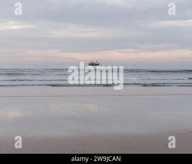 Naviga verso il mare al tramonto con nuvole che si riflettono sulla spiaggia di sabbia bagnata in una serata d'inverno nella città di Essaouira, in Marocco. 28 dicembre 2023 Foto Stock