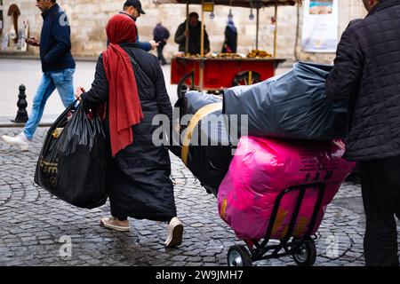 Donna che trasporta e traina grandi carichi in strada. Una donna porta con sé un sacco pesante pieno di cose, in mano e su un carrello. Istanbul Turchia-20 dicembre, Foto Stock