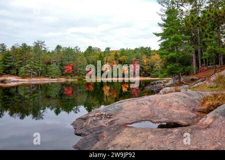 Alberi colorati in autunno circondati da verdi pini si riflettono nell'acqua del Silent Lake Provincial Park con il granito dello sciame canadese Foto Stock