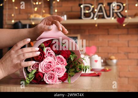 Donna con bouquet di belle rose su un tavolo di legno, primo piano. Festa di San Valentino Foto Stock