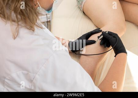 Medico che esegue la procedura di elettrolisi di depilazione sulla gamba della donna, Shin. Epilazione elettrica nel salone di bellezza. Piano orizzontale. Foto autentica Foto Stock