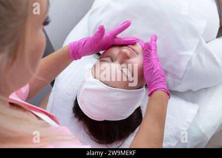 Vista dall'alto della bellissima ragazza caucasica durante la procedura di pulizia, idratazione della pelle del viso, massaggio facciale. Estetista professionista in Foto Stock