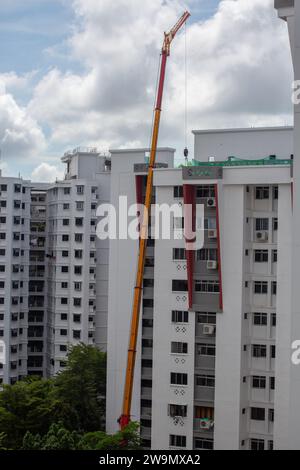 I lavori industriali impiegano una gru per il sollevamento di merci pesanti o attrezzature per lo scarico sul tetto di un edificio residenziale, Singapore. Foto Stock