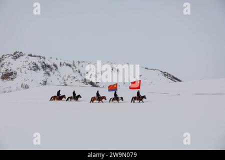 ALTAY, CINA - 29 DICEMBRE 2023 - agenti di polizia in una stazione di polizia di frontiera pattugliano a cavallo con bandiere nazionali nella zona di frontiera del confine Foto Stock