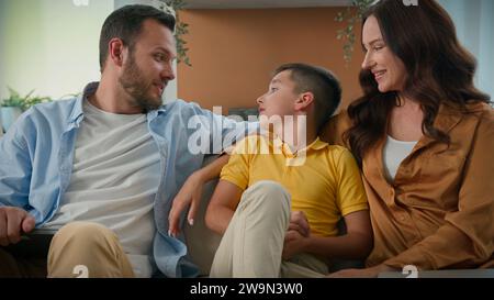 Famiglia caucasica felice che si rilassa a casa durante il fine settimana genitori amorevoli, mamma, papà, comunicano con il figlio, il bambino, che si abbraccia su un comodo divano Foto Stock