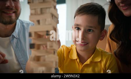 Primo piano: Mamma, papà e figlio di famiglia caucasica felici che si divertono a giocare con i genitori di Jenga che giocano con l'amato bambino in un gioco da tavolo logico intellettuale Foto Stock